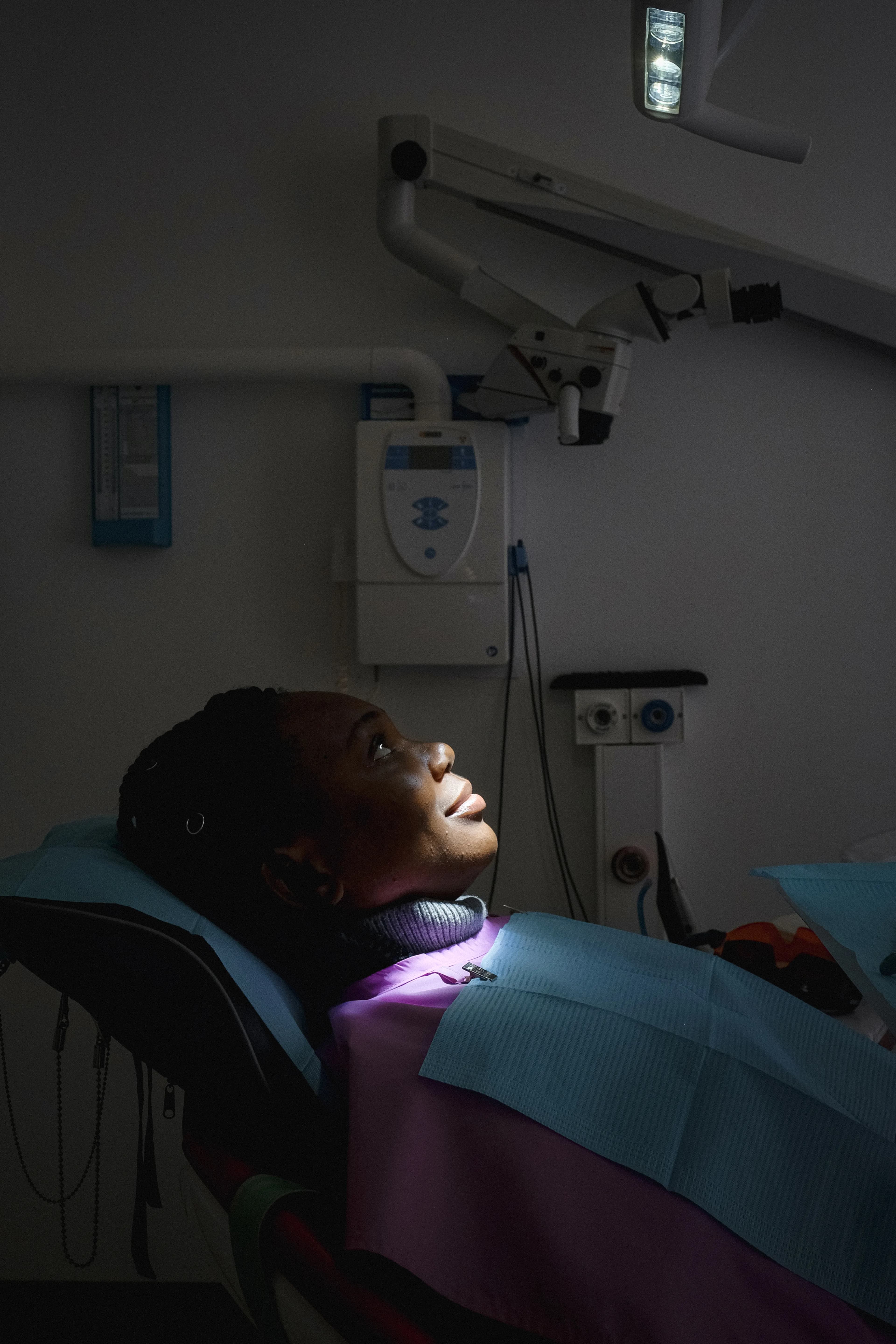 Patiente assise dans un fauteuil de soins dentaires, dans une salle peu éclairée.